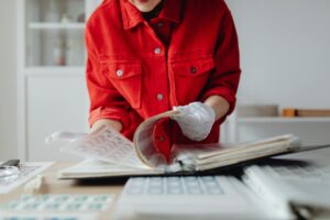 Close-up of a person wearing gloves and a red jacket flipping through a stamp album indoors.